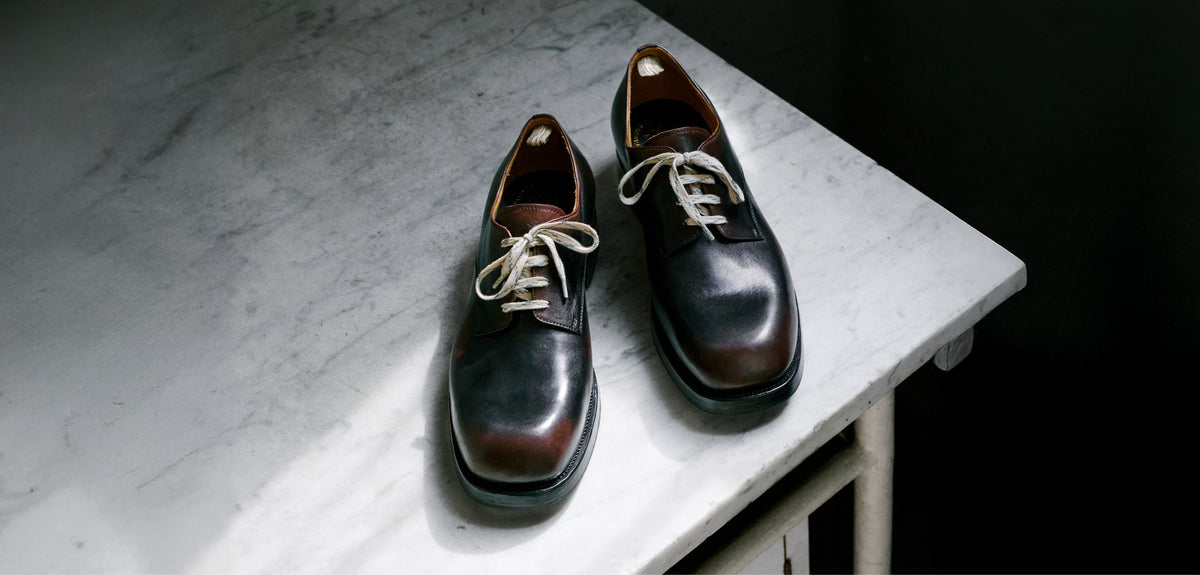 A pair of men's dark brown leather lace-up dress shoes with white laces, displayed on a white marble tabletop against a dark background.